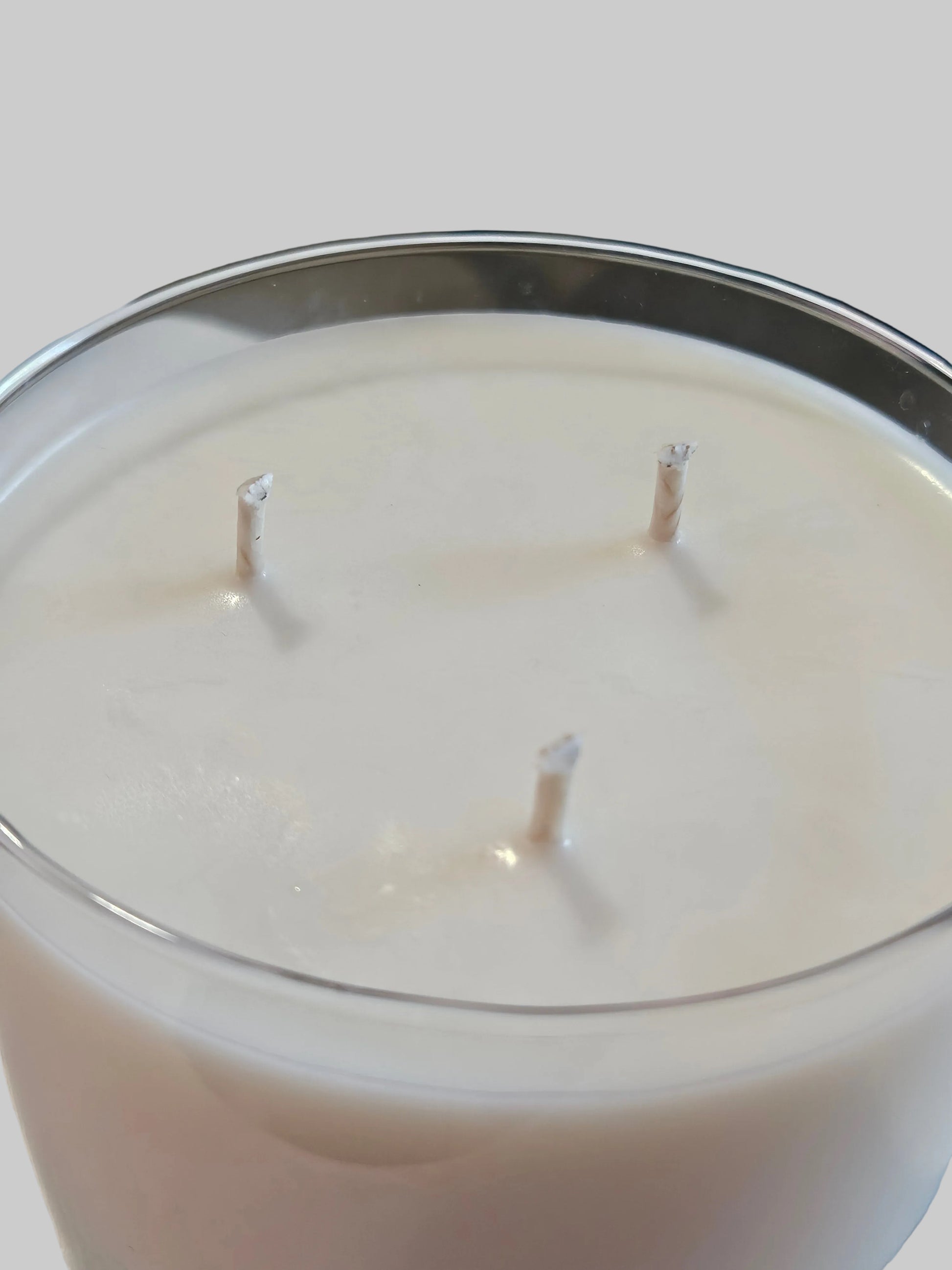 A close-up of a white wax candle in a clear glass vessel with three visible wicks