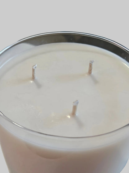 A close-up of a white wax candle in a clear glass vessel with three visible wicks